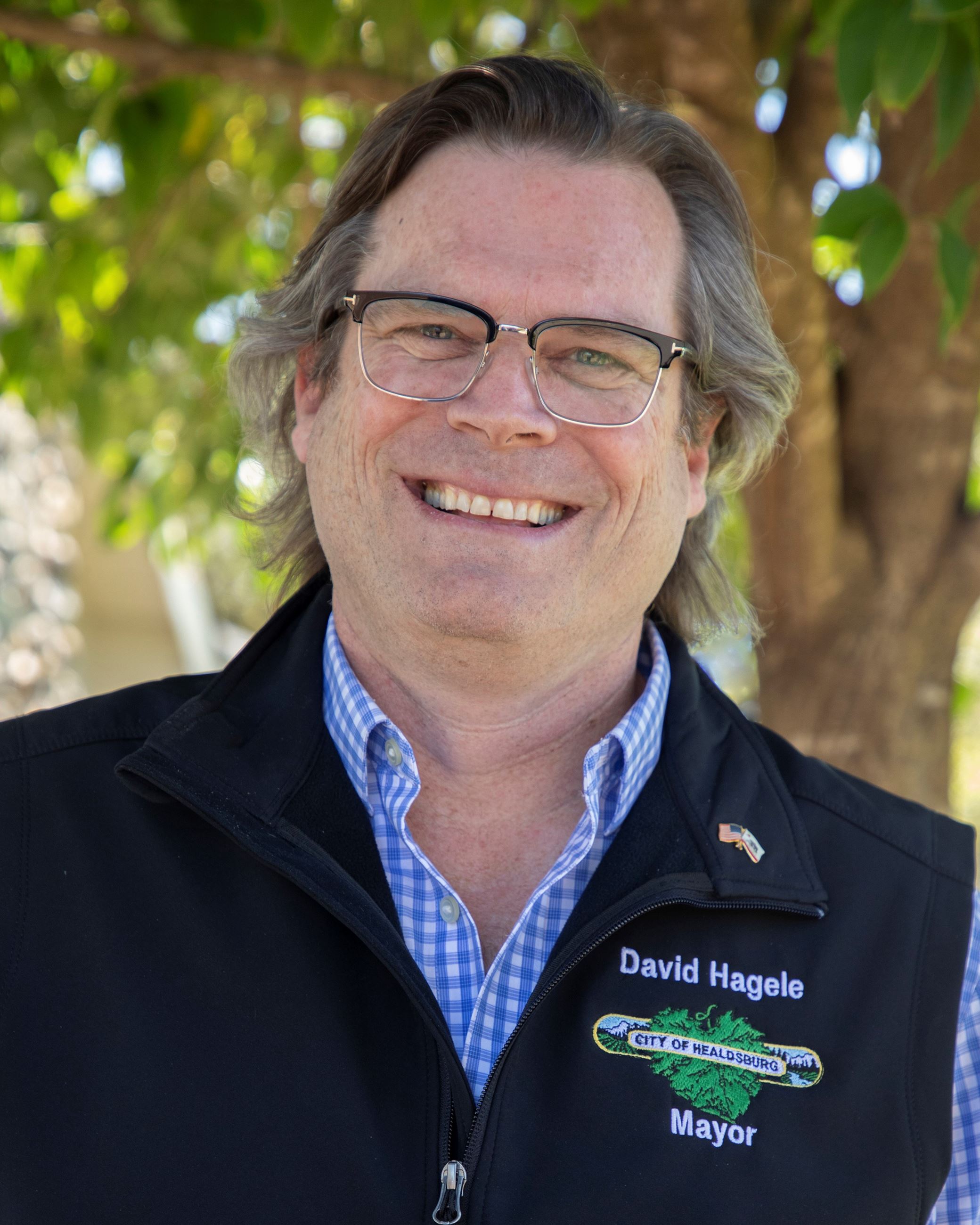Councilmember David Hagele standing in front of a green tree wearing a black vest
